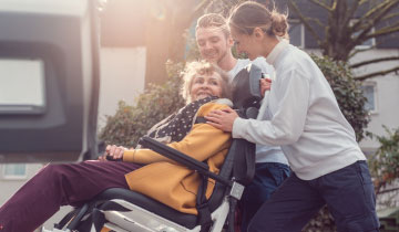 Zwei freundliche medizinische Helfer befördern eine ältere Dame im Tragestuhl in einen Krankentransporter
