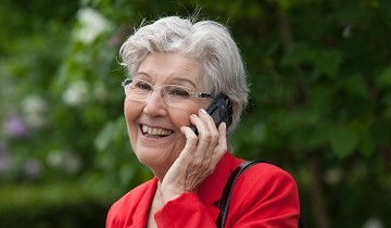 Ältere Frau hält Handy mit Seniorennotruf ans Ohr und lacht