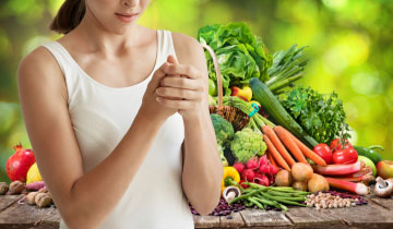 Eine junge Frau steht mit schmerzenden arthritischen Fingern vor einem Berg von Obst und Gemüse