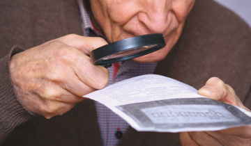 Ein Senior versucht mithilfe einer Lesehilfe Kleingedrucktes zu entziffern